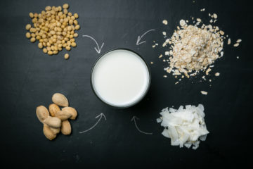 A glass of plant based milk-along with soy, oats, nuts and coconut- on black background