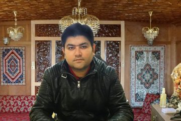 Sahil Verma, Founder of PureMart, sitting in a Kashmiri living room, with Kashmiri rugs behind him and chandeliers above him