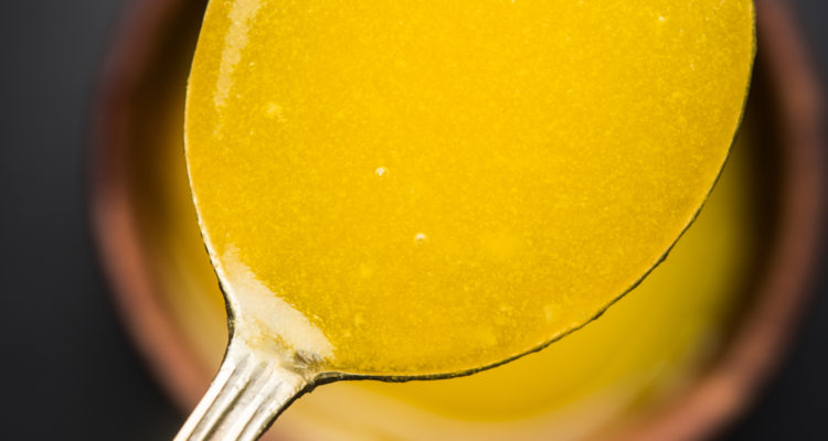 Ghee or clarified butter close up in wooden bowl and silver spoon, selective focus